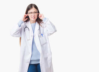 Young Chinese doctor woman over isolated background covering ears with fingers with annoyed expression for the noise of loud music. Deaf concept.