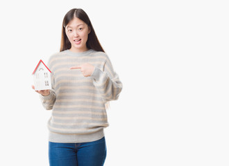 Young Chinese real state agent woman over isolated background holding house very happy pointing with hand and finger