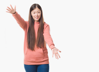 Young Chinese woman over isolated background wearing sport sweathshirt looking at the camera smiling with open arms for hug. Cheerful expression embracing happiness.