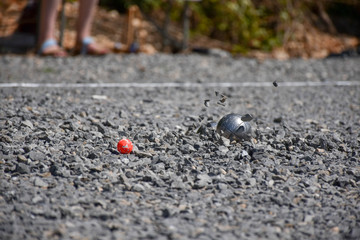 Closeup of a steel ball for petanque hitting the gravel surface, pieces flying, with the cochonet visible