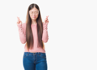 Fototapeta na wymiar Young Chinese woman over isolated background wearing glasses smiling crossing fingers with hope and eyes closed. Luck and superstitious concept.