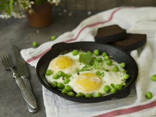 Delicious breakfast - fried eggs with green peas. On a dark background. Close up, copy space