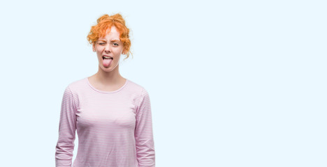 Young redhead woman sticking tongue out happy with funny expression. Emotion concept.