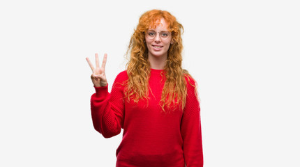 Obraz na płótnie Canvas Young redhead woman wearing red sweater showing and pointing up with fingers number three while smiling confident and happy.
