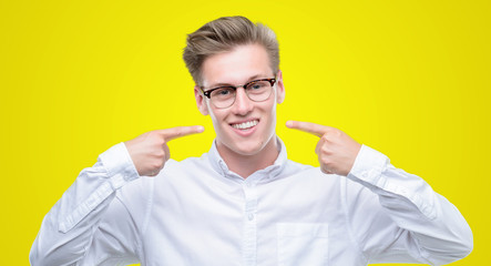 Young handsome blond man smiling confident showing and pointing with fingers teeth and mouth....