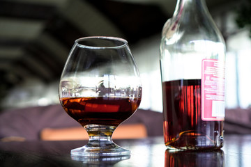 A glass of cognac on a black table with a bottle of cognac in the background.