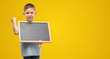Dark haired little child holding a blackboard annoyed and frustrated shouting with anger, crazy and yelling with raised hand, anger concept