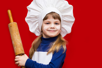 Happy little girl in chef uniform holds rolling pin isolated on light background. Kid chef. Cooking Process Concept 
