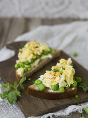 Bruschetta with green peas, cheese and egg on a wooden board. Close up, copy space