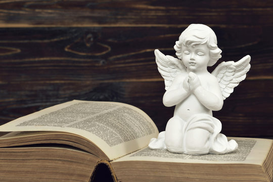 Condolence card with a guardian angel kneeling and praying on open book
