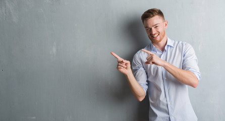 Young redhead business man over grey grunge wall smiling and looking at the camera pointing with two hands and fingers to the side.