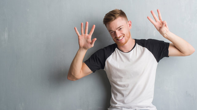 Young redhead man over grey grunge wall showing and pointing up with fingers number eight while smiling confident and happy.