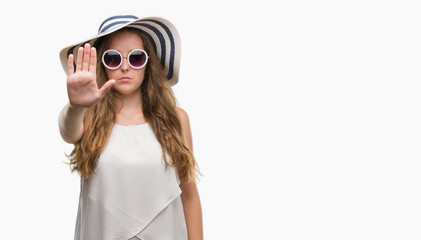 Young blonde woman wearing sunglasses and summer hat with open hand doing stop sign with serious...