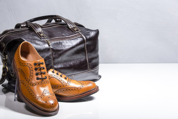 Male Tanned Full Broggued Oxford Calf Leather Shoes Along With Dakr Brown Leather Travel Bag on White Surface.