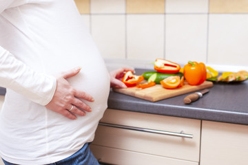 Closeup of Pregnant Female with Palm on Stomach Making a Salad with Vegetables on Kitchen.