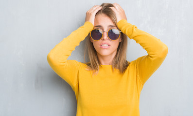 Beautiful young woman standing over grunge grey wall wearing retro sunglasses stressed with hand on head, shocked with shame and surprise face, angry and frustrated. Fear and upset for mistake.