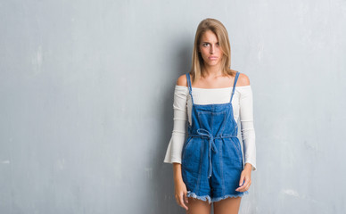 Beautiful young woman standing over grunge grey wall skeptic and nervous, frowning upset because of...