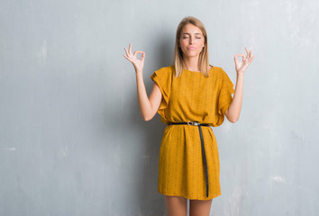 Beautiful young woman standing over grunge grey wall wearing a dress relax and smiling with eyes closed doing meditation gesture with fingers. Yoga concept.