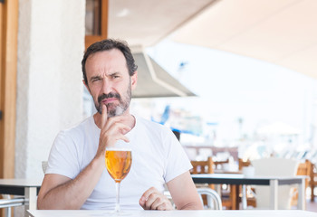 Handsome senior man drinking beer at restaurant serious face thinking about question, very confused idea
