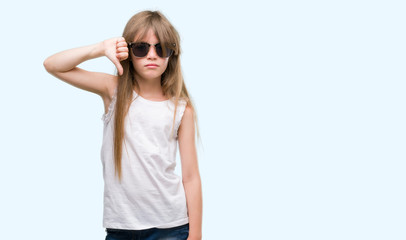 Young blonde toddler wearing sunglasses with angry face, negative sign showing dislike with thumbs down, rejection concept