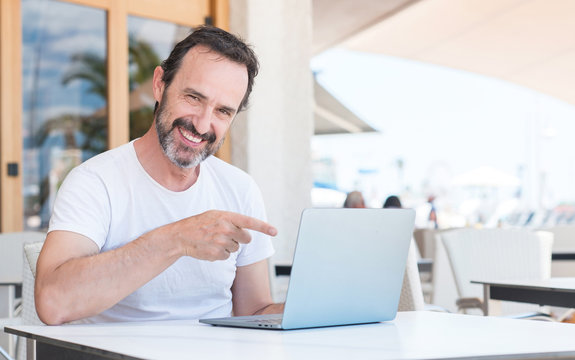 Handsome senior man using laptop at restaurant very happy pointing with hand and finger