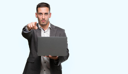 Handsome young man using computer laptop pointing with finger to the camera and to you, hand sign, positive and confident gesture from the front