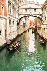 Obraz na płótnie Canvas Gondolier carrying tourists in their gondola, by the bridge of sighs in venice, italy at sunset