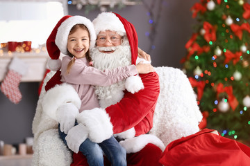 Fototapeta na wymiar Little girl sitting on authentic Santa Claus' lap indoors