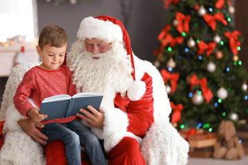 Fototapeta na wymiar Little boy reading book while sitting on authentic Santa Claus' lap indoors