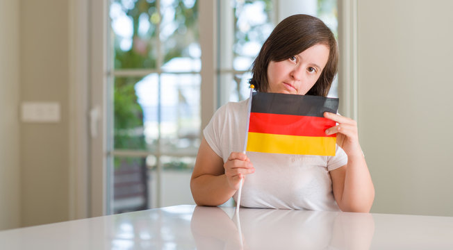 Down syndrome woman at home holding flag of germany with a confident expression on smart face thinking serious