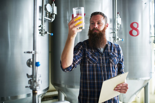 brewer checking beer for qaulity at brewery while holding clipboard