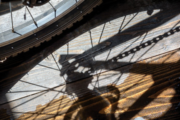 Rear wheel of a cycle with the chain and gear cogs in reflected shadow with a puddle of water creating an art reflection