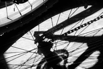 Rear wheel of a cycle with the chain and gear cogs in reflected shadow with a puddle of water creating an art reflection in black and white