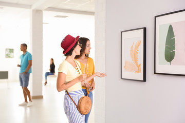 Young women at exhibition in art gallery - obrazy, fototapety, plakaty