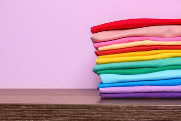 Stack of colorful t-shirts on table against color background