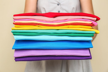 Woman holding stack of colorful t-shirts on light background