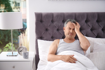 Man suffering from headache after sleep in bed. Uncomfortable pillow