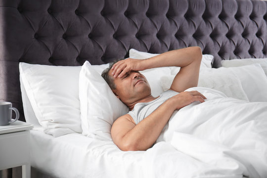 Man suffering from headache after sleep in bed. Uncomfortable pillow