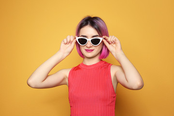Young woman with trendy hairstyle wearing sunglasses against color background