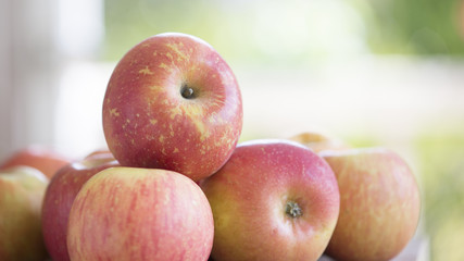 Fresh fuji apples piled on a butcher block in front of an open door.  Sunny day outside.