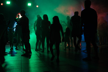 People dance at a nightclub at night in silhouette with different color lights and digital effects