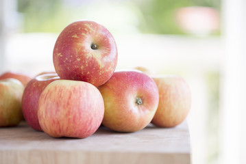 Fresh fuji apples piled on a butcher block in front of an open door.  Sunny day outside.