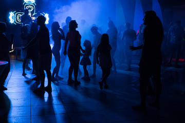 People dance at a nightclub at night in silhouette with different color lights and digital effects