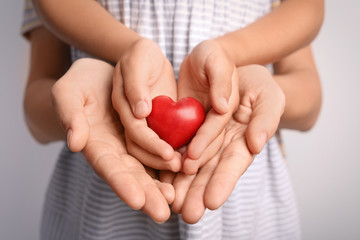 Family holding small red heart in hands together, closeup