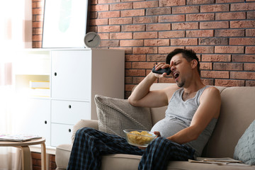 Lazy man with bowl of chips sitting on sofa at home