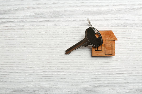 Key with trinket in shape of house on wooden background. Real estate agent services