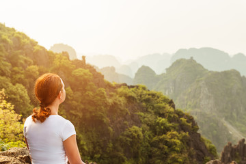 Naklejka premium back view woman tourist looking far away and enjoying valley and hills view from top of a mountain