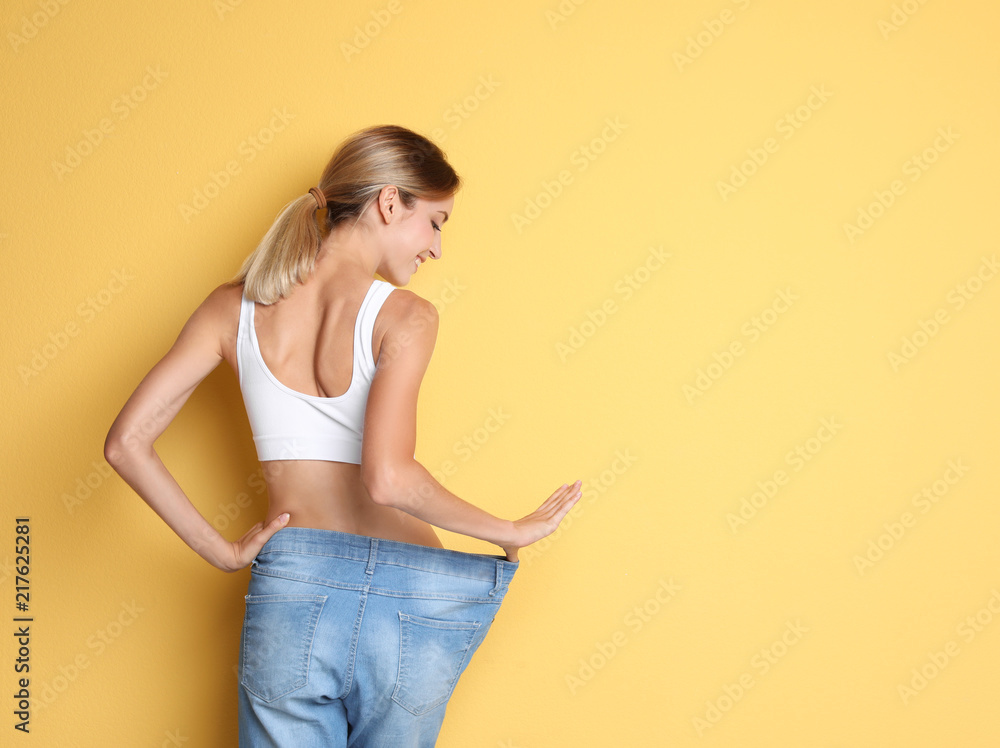 Canvas Prints Young slim woman in old big jeans showing her diet results on color background