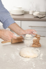 Man sprinkling dough for pastry with flour on table