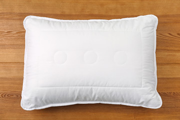 Soft bed pillow on wooden background, top view